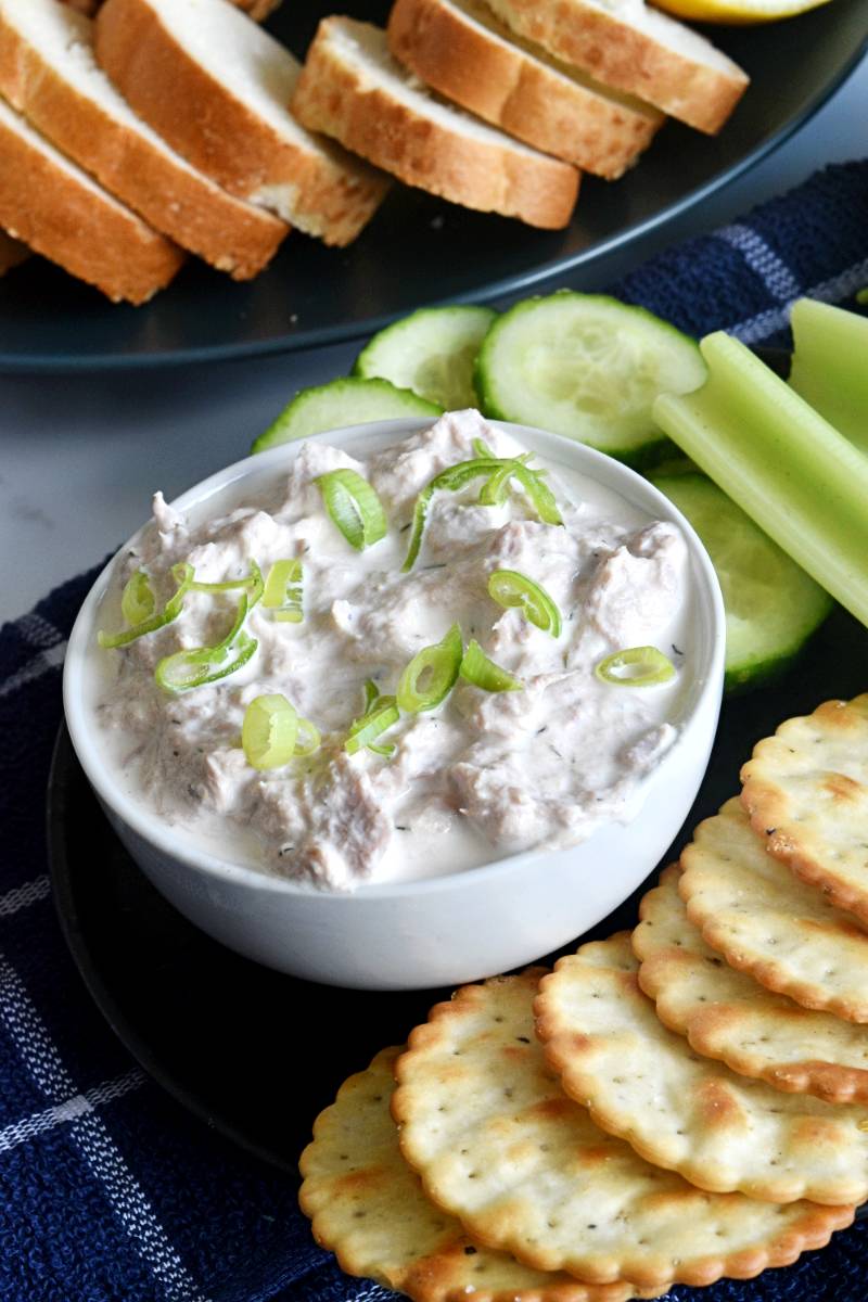 Tuna cream cheese dip on a table with cucumbers, celery sticks, bread and crackers.