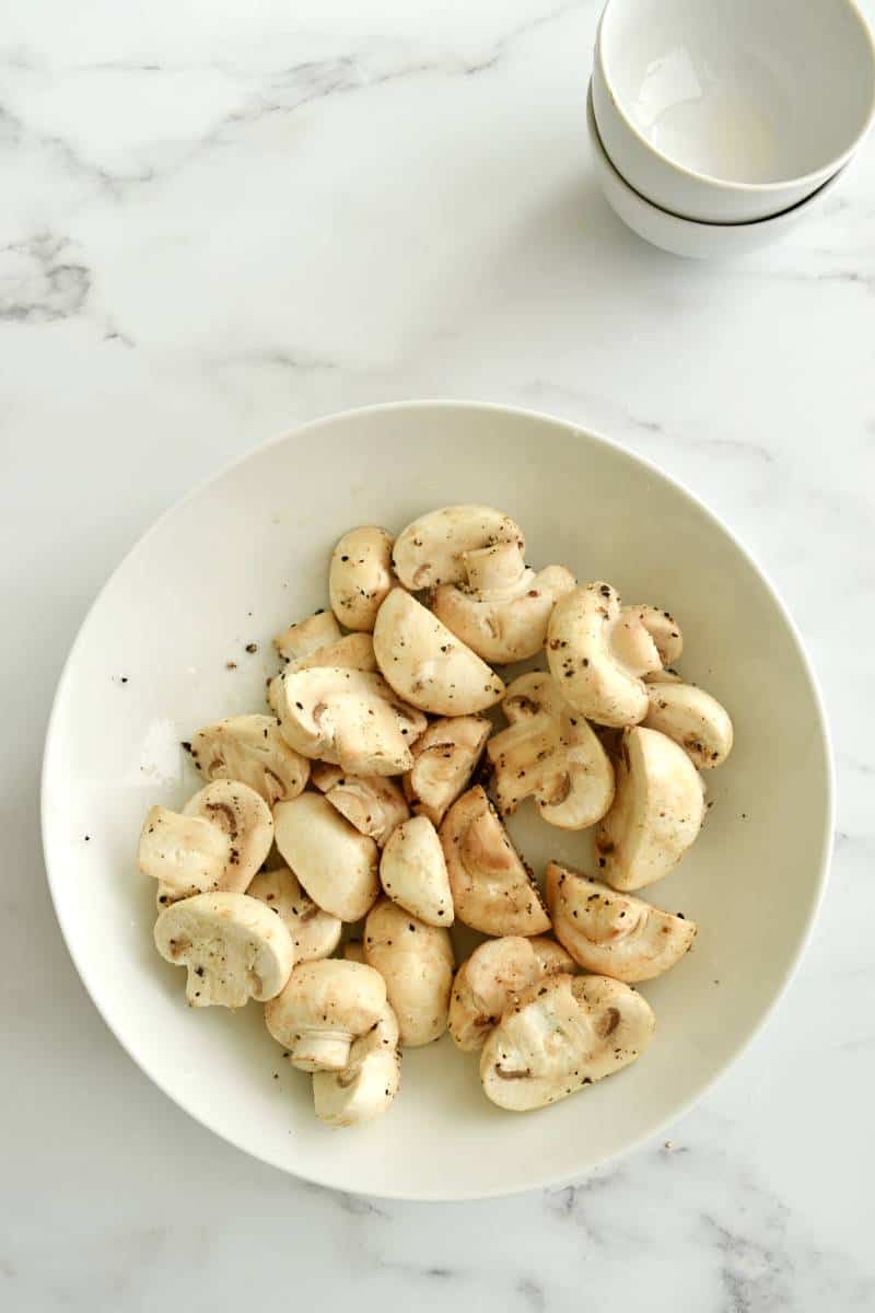 Uncooked mushrooms with seasoning in a bowl.