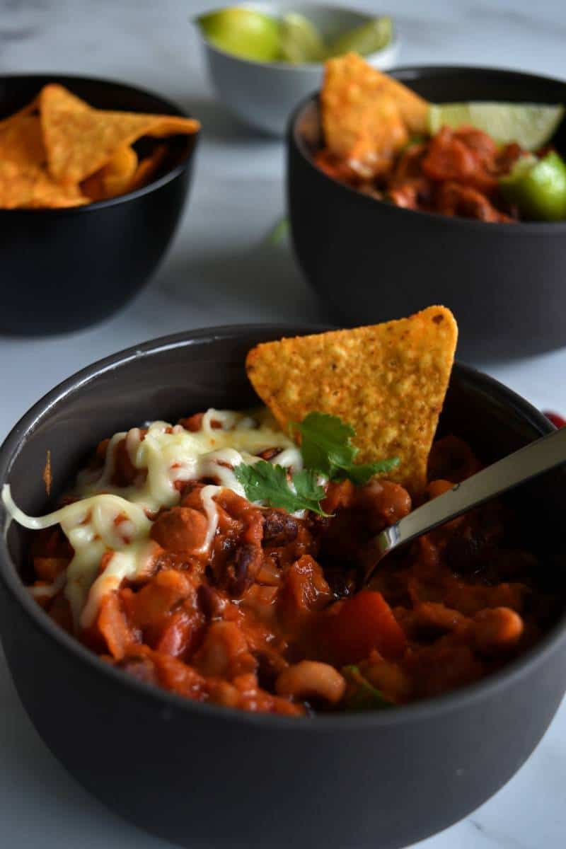 Vegan chilli in a bowl with cheese and tortilla chip on top.