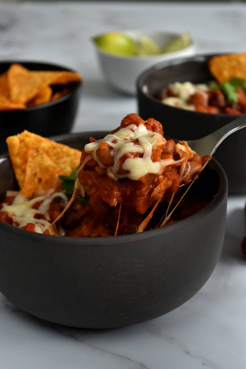 Veggie chilli with cheese, a spoonful lifting up a cheesy bite.