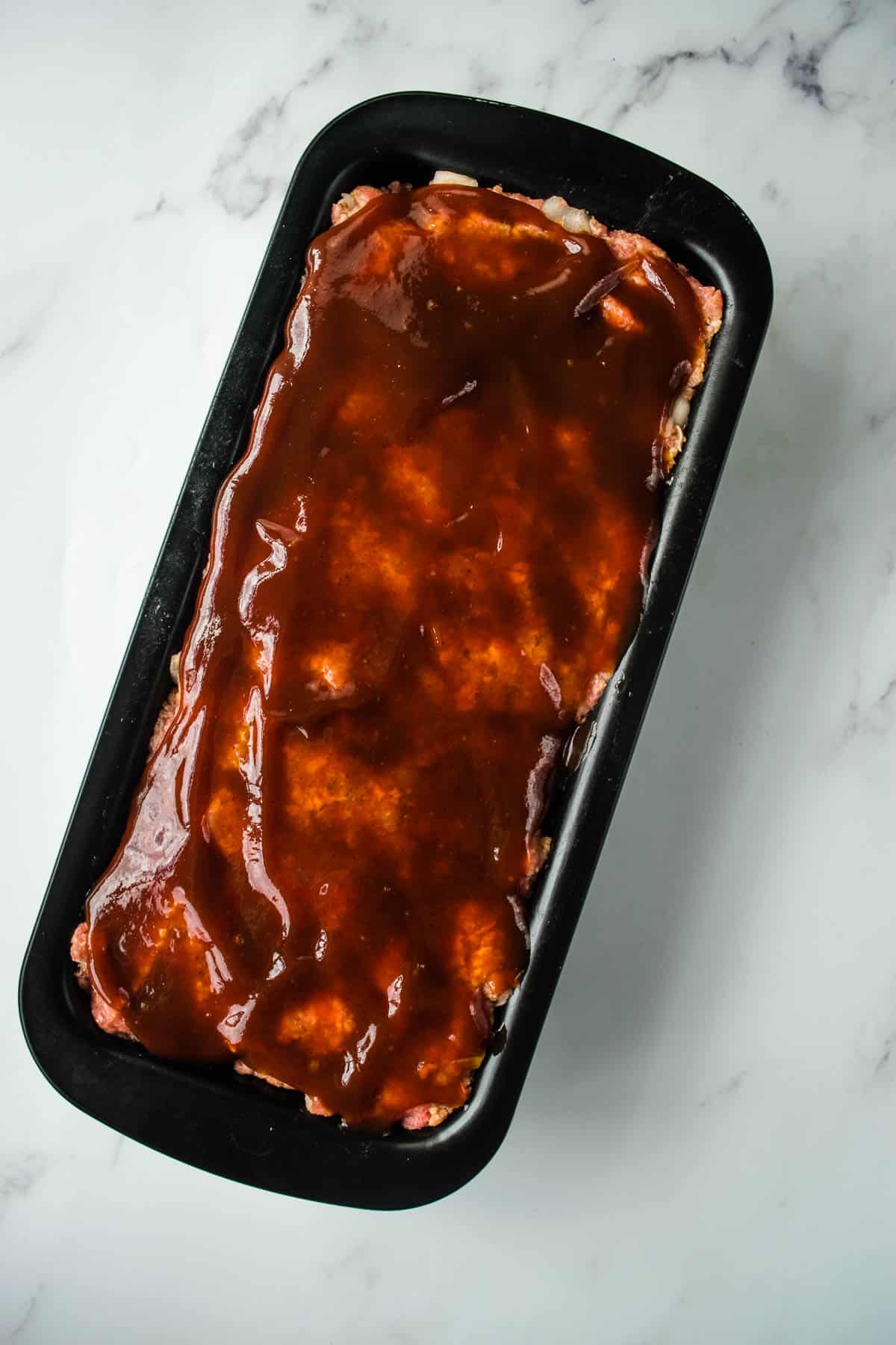 Uncooked meatloaf with BBQ sauce on top.