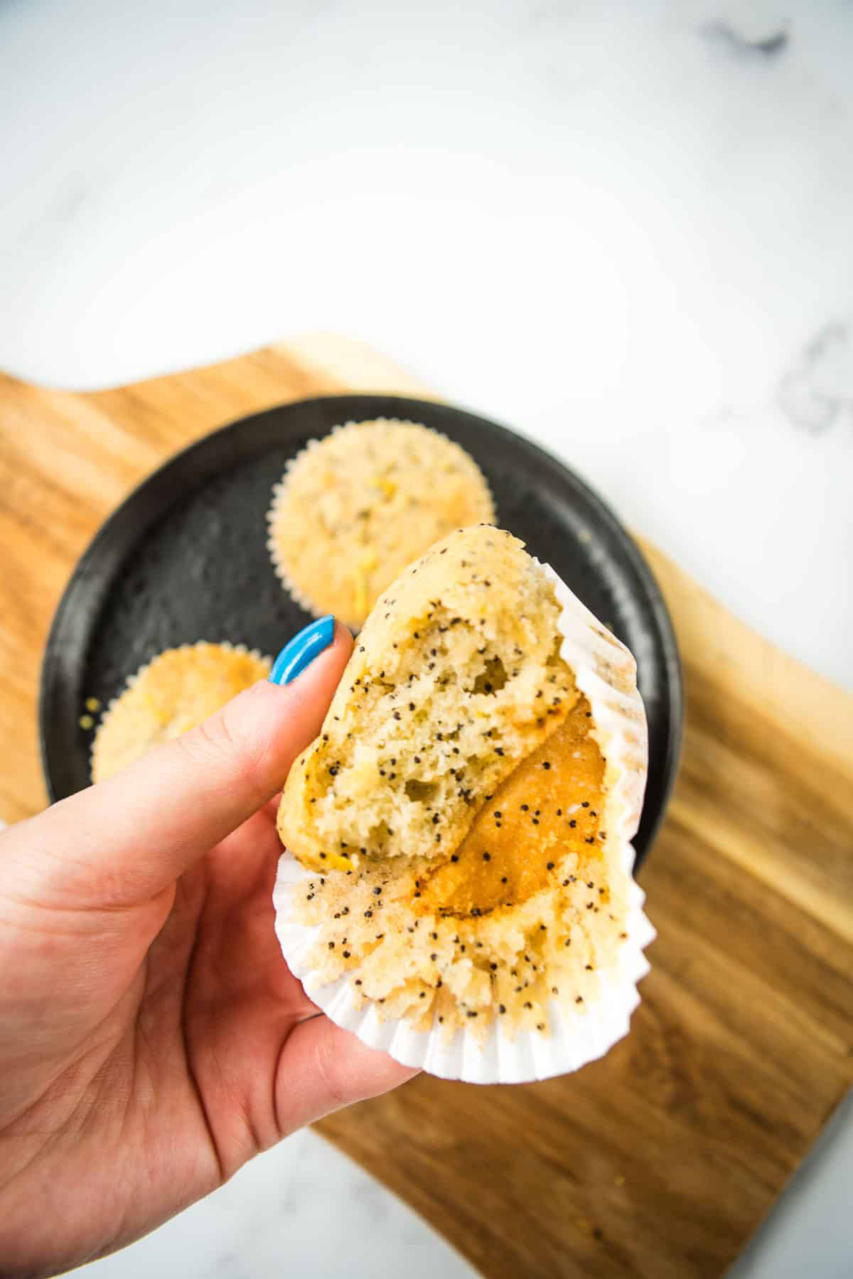 A hand holding a muffin with a bite taken out of it.