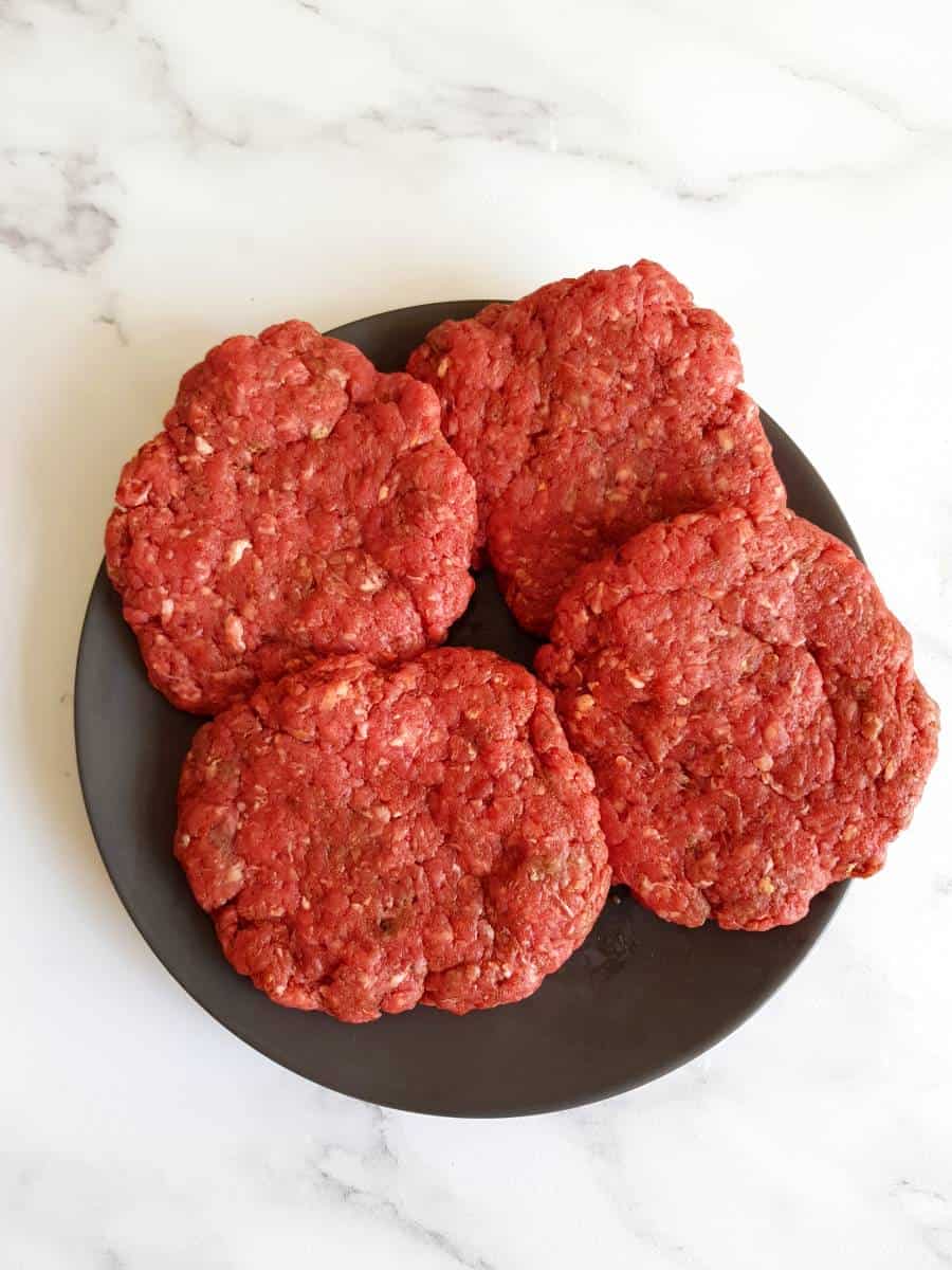 Raw beef burgers on a plate.