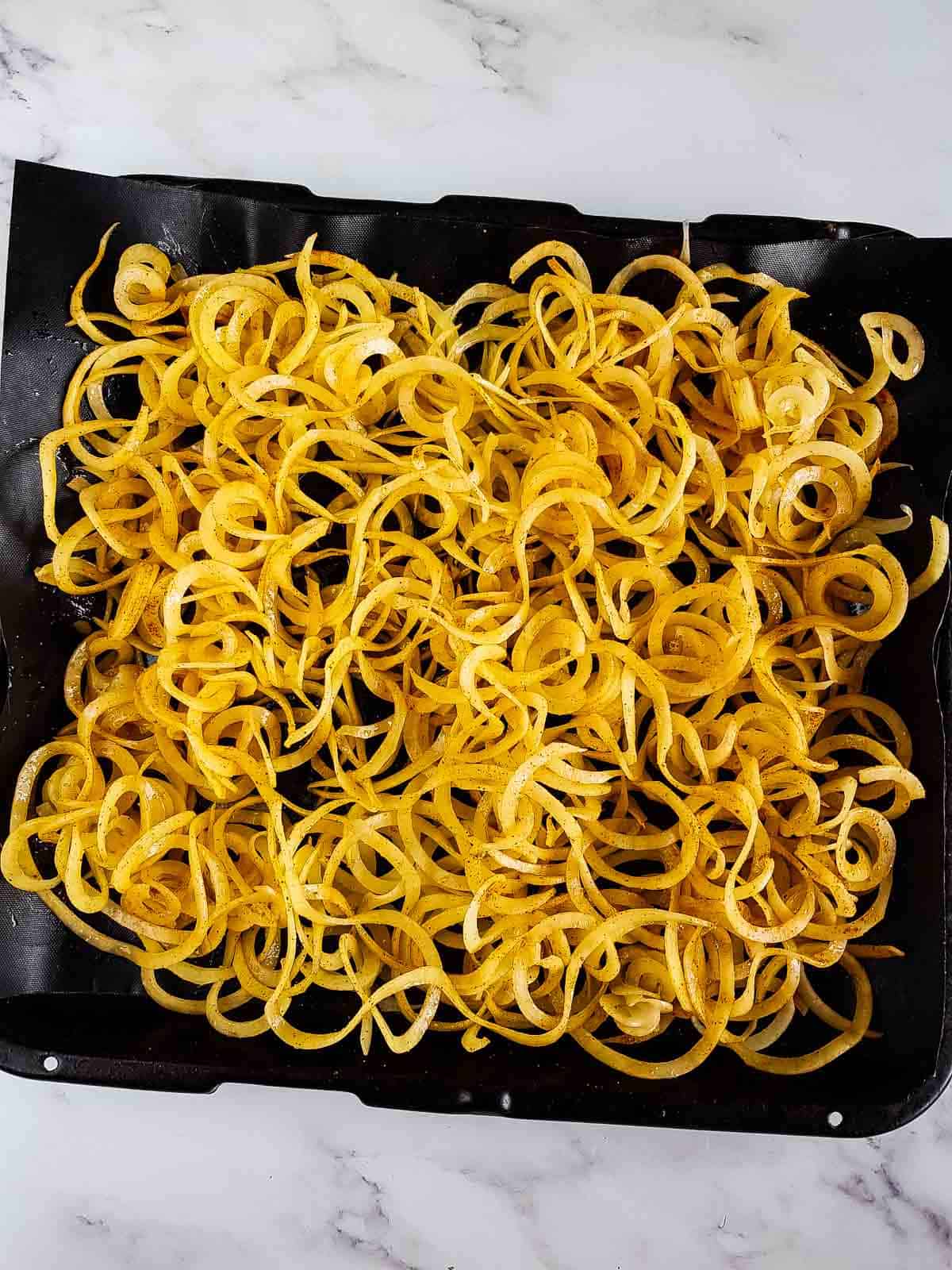Seasoned potato spirals on a sheet pan.