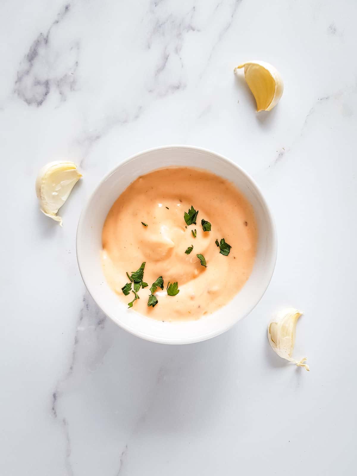 Sriracha aioli in a bowl surrounded by garlic cloves.