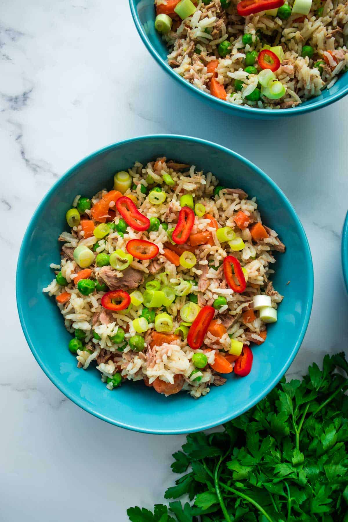 A bowl of fried rice with tuna, carrots, peas and chili.