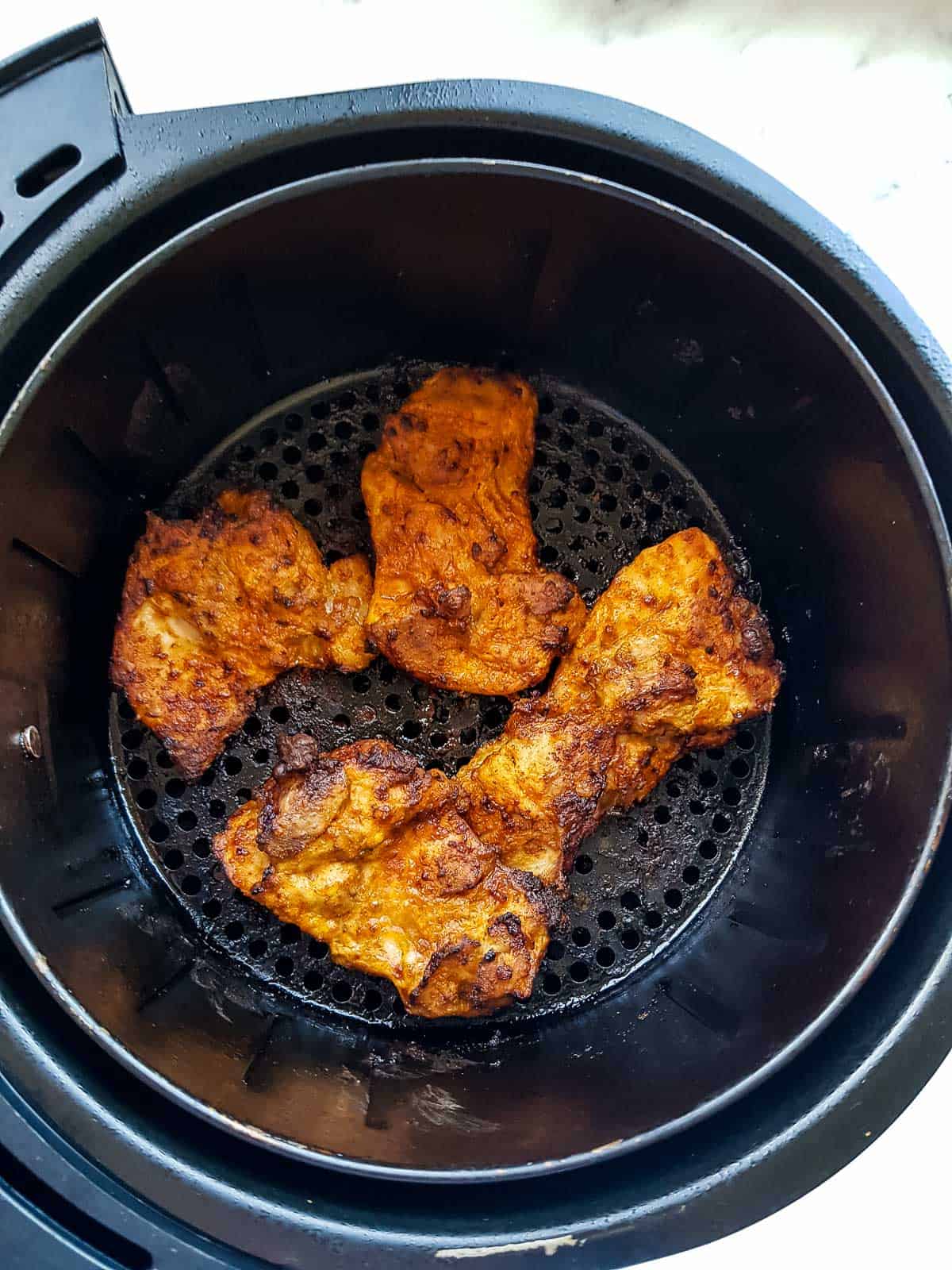 Cooked chicken thighs in an air fryer.