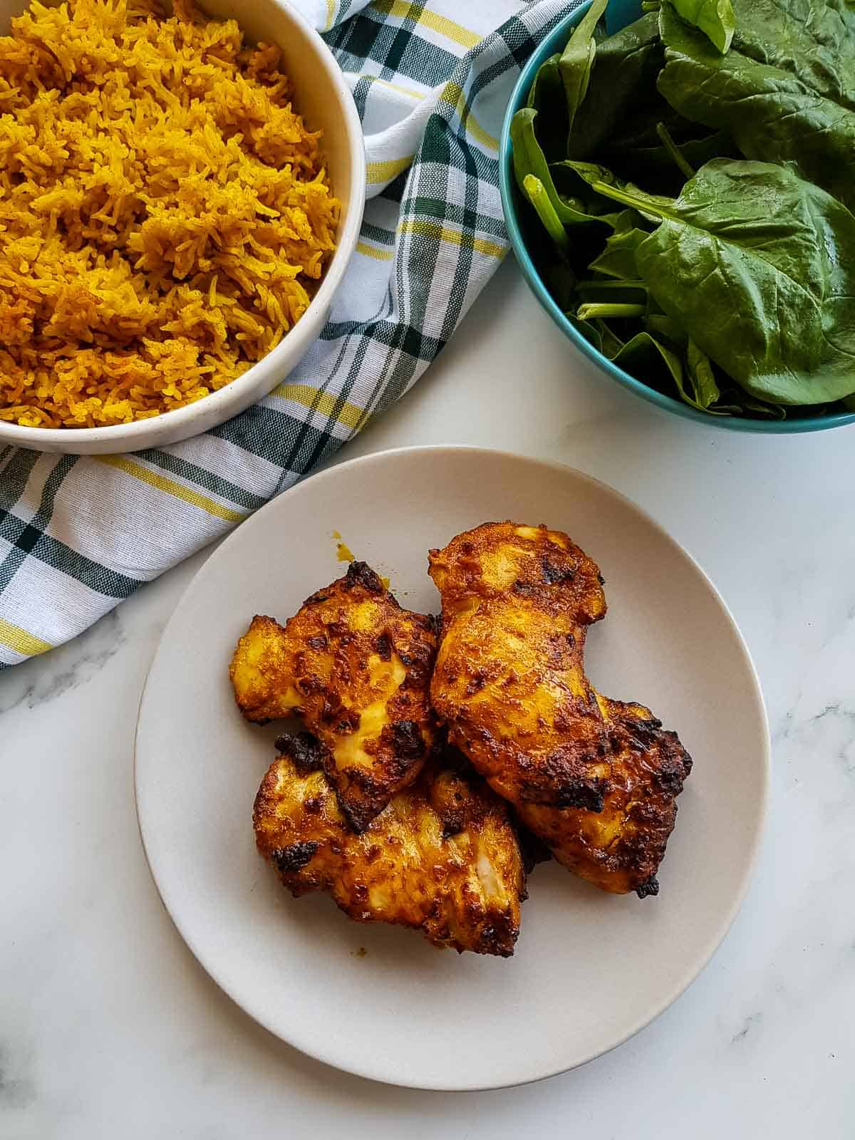 Chicken thighs on a plate with rice and salad on the side.