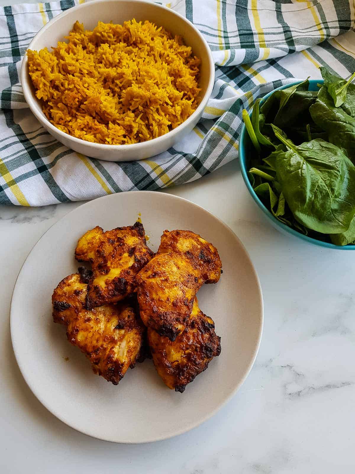 Chicken thighs on a plate with rice and salad in the background.