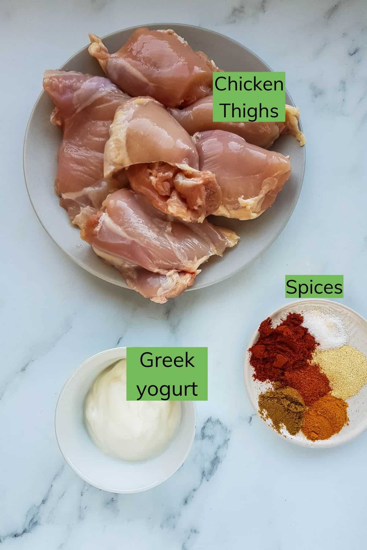 Greek yogurt, chicken thighs and spices laid out on a table.