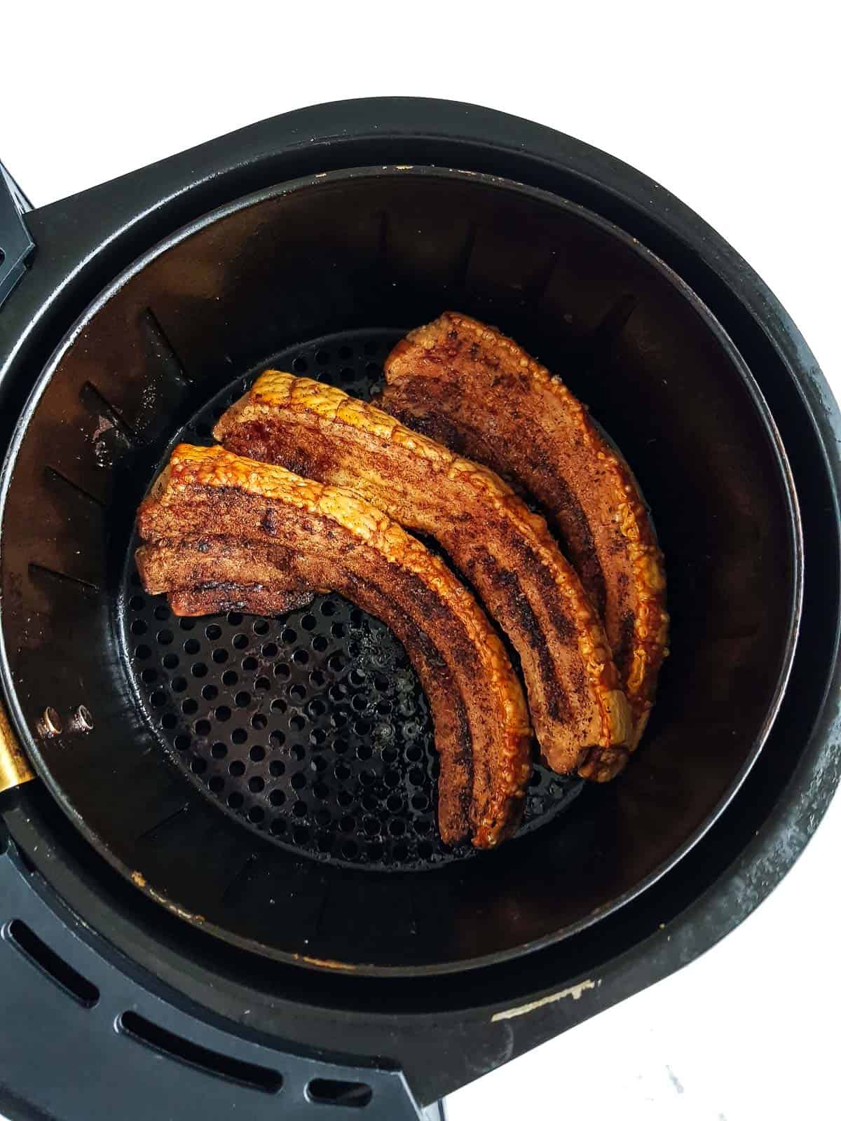 Pork belly slices in an air fryer basket.