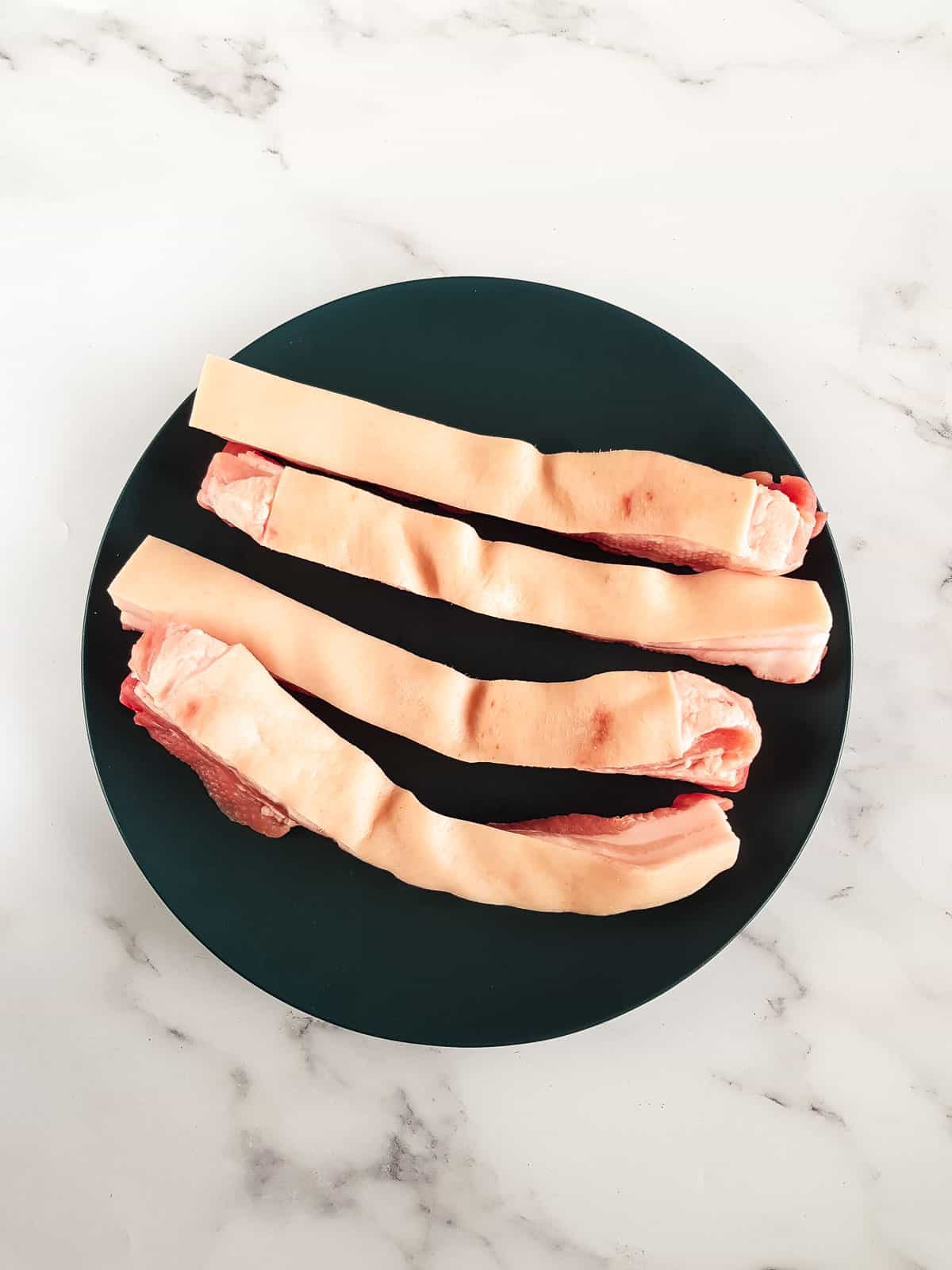 Raw pork belly slices on a plate.