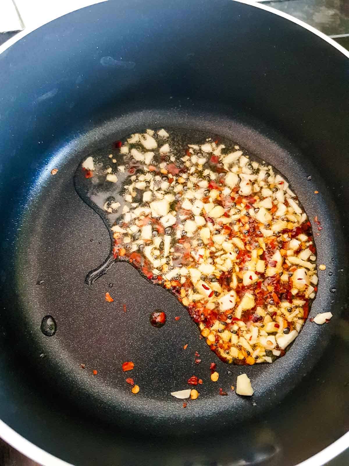 Chopped garlic and red pepper flakes sautéing in a pot.