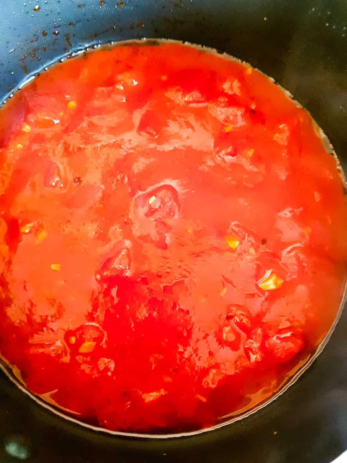 Diced tomatoes added to the chili and pepper flakes.