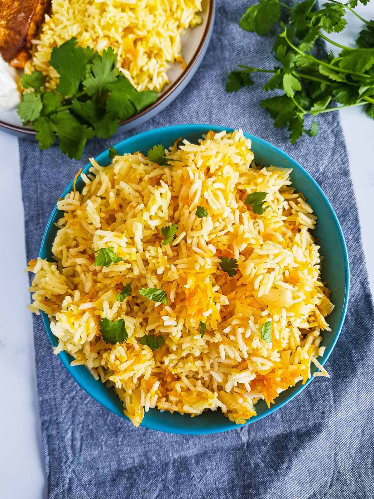 Bowl of carrot rice with a plate of food in the background.