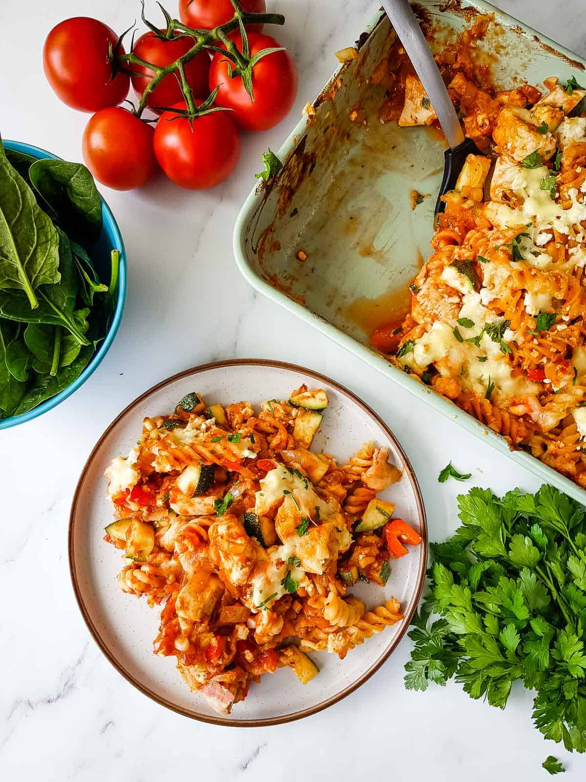 Served portion of chicken and bacon pasta bake, with salad and tomatoes on the side.