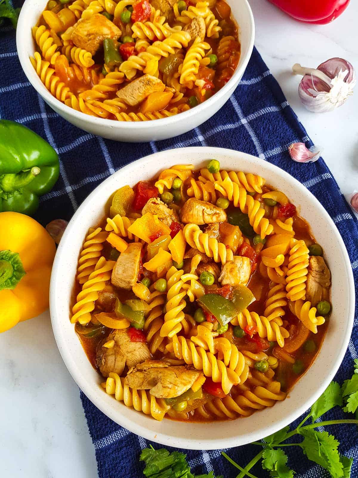 Two bowls of pasta with ingredients on the side.