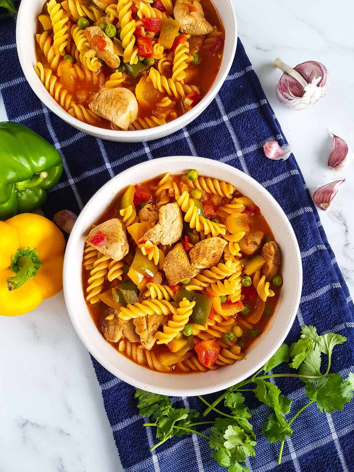 Two bowls of chicken curry pasta with ingredients scattered.
