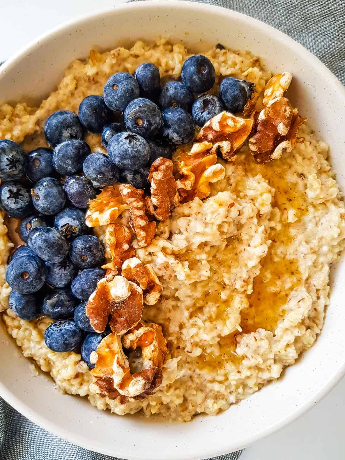 A white bowl with oatmeal, blueberries and walnuts.