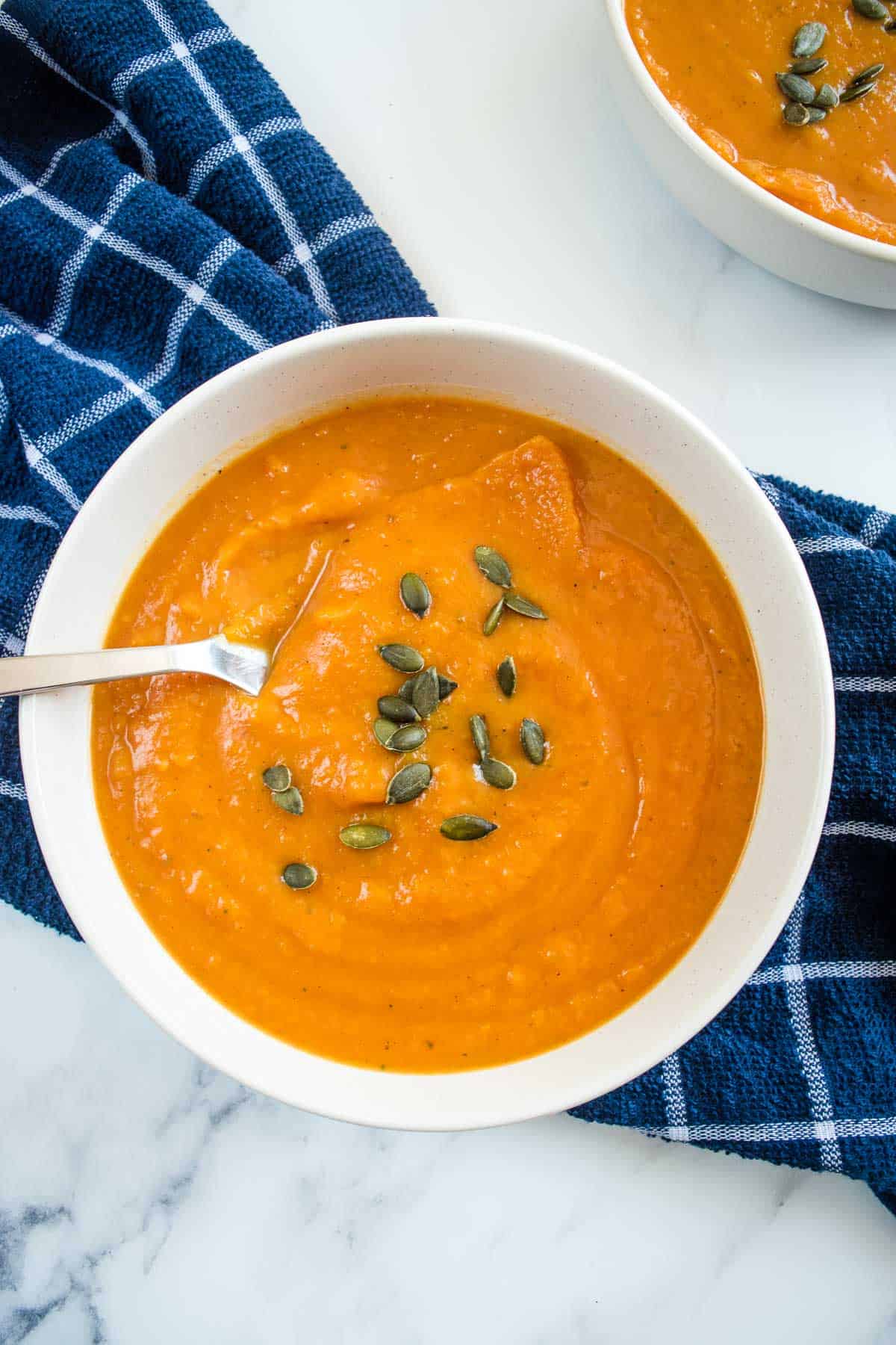 Pumpkin and Sweet Potato Soup topped with pumpkin seeds in a bowl with a spoon in it.