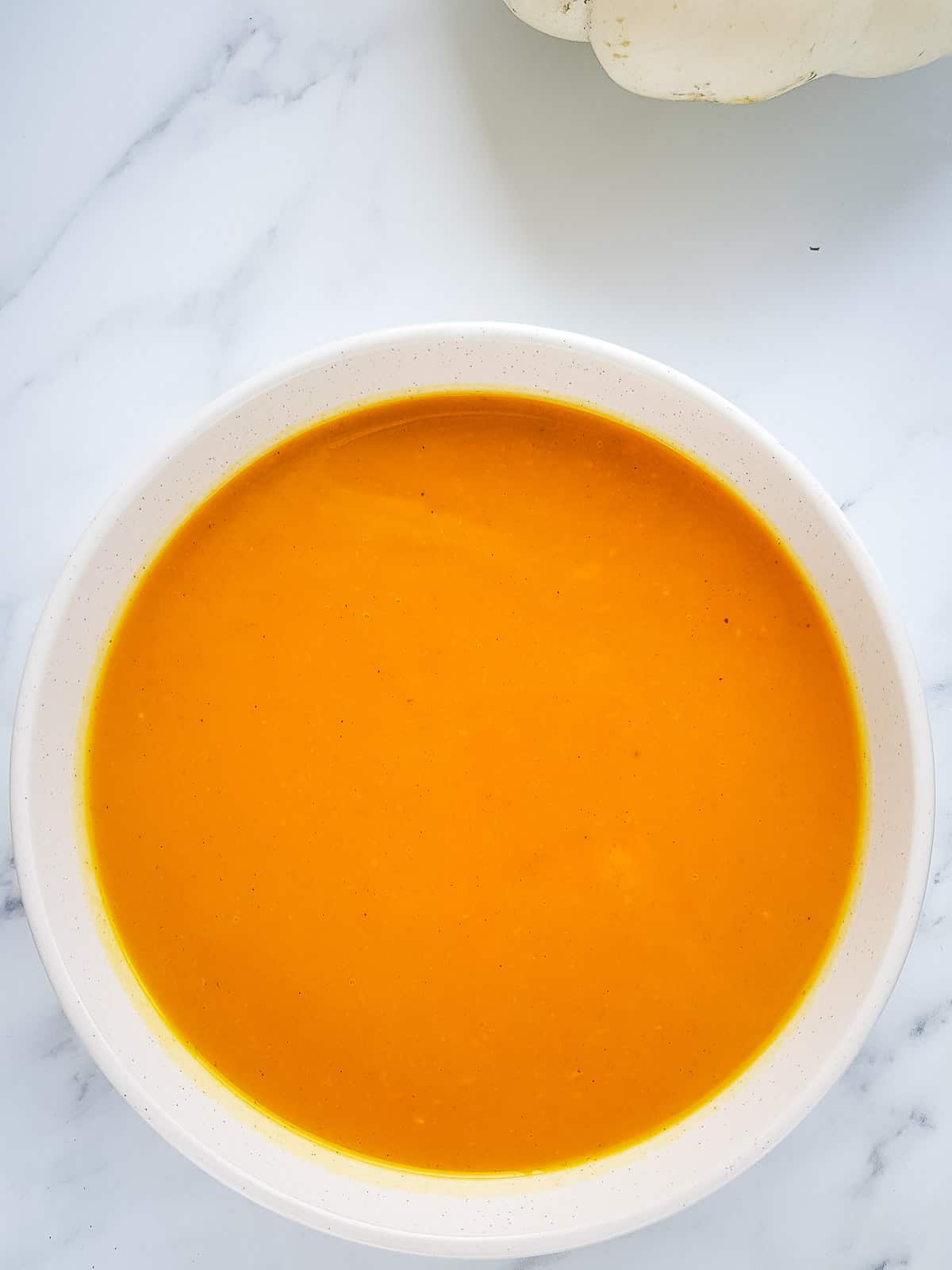 A white bowl with pumpkin soup.