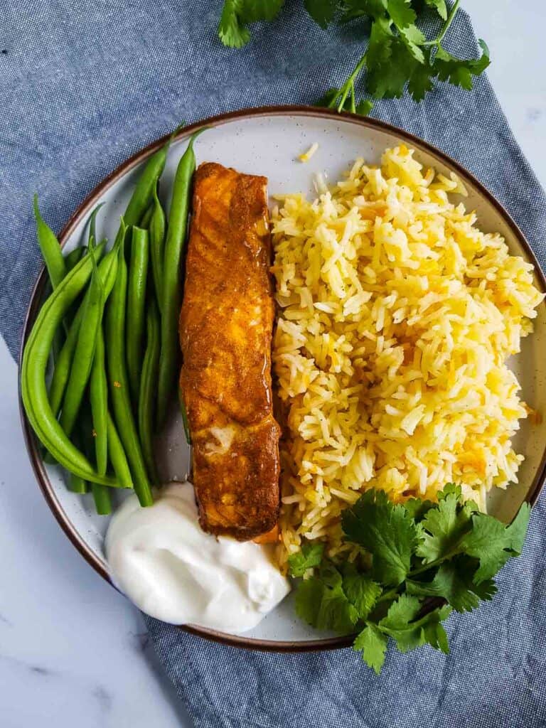 A plate with tandoori salmon, carrot rice and green beans.