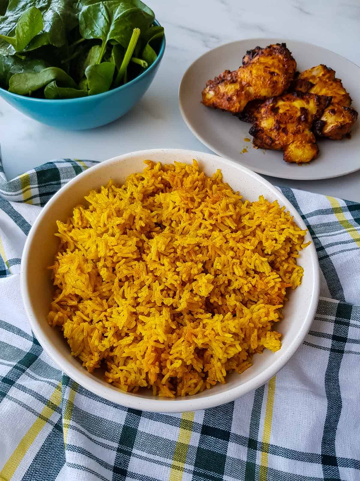 Turmeric rice on a table with chicken and salad.