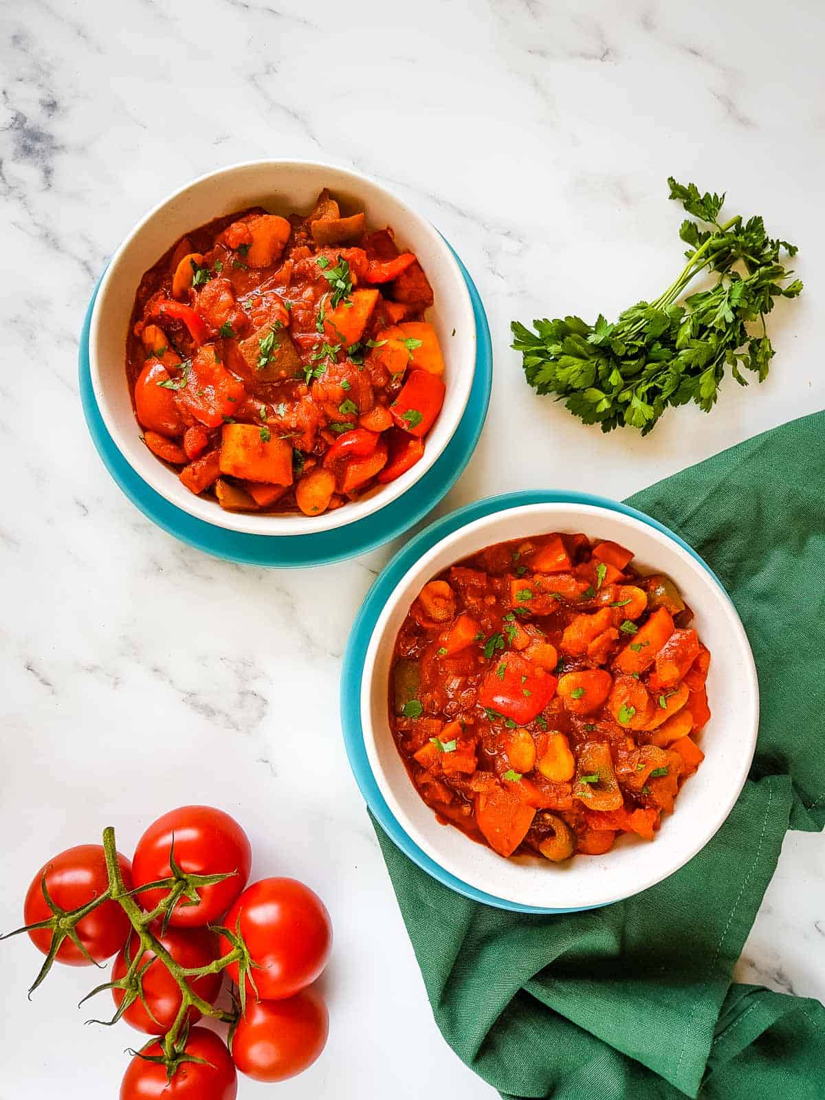 Vegetable goulash in bowls with parsley and tomatoes on the side.