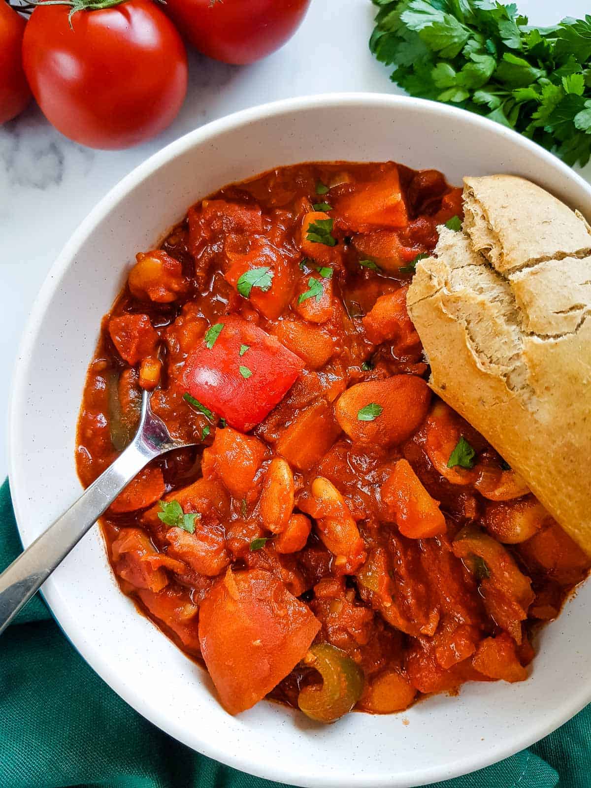 Goulash in a bowl with a spoon in it, a baguette on the side.