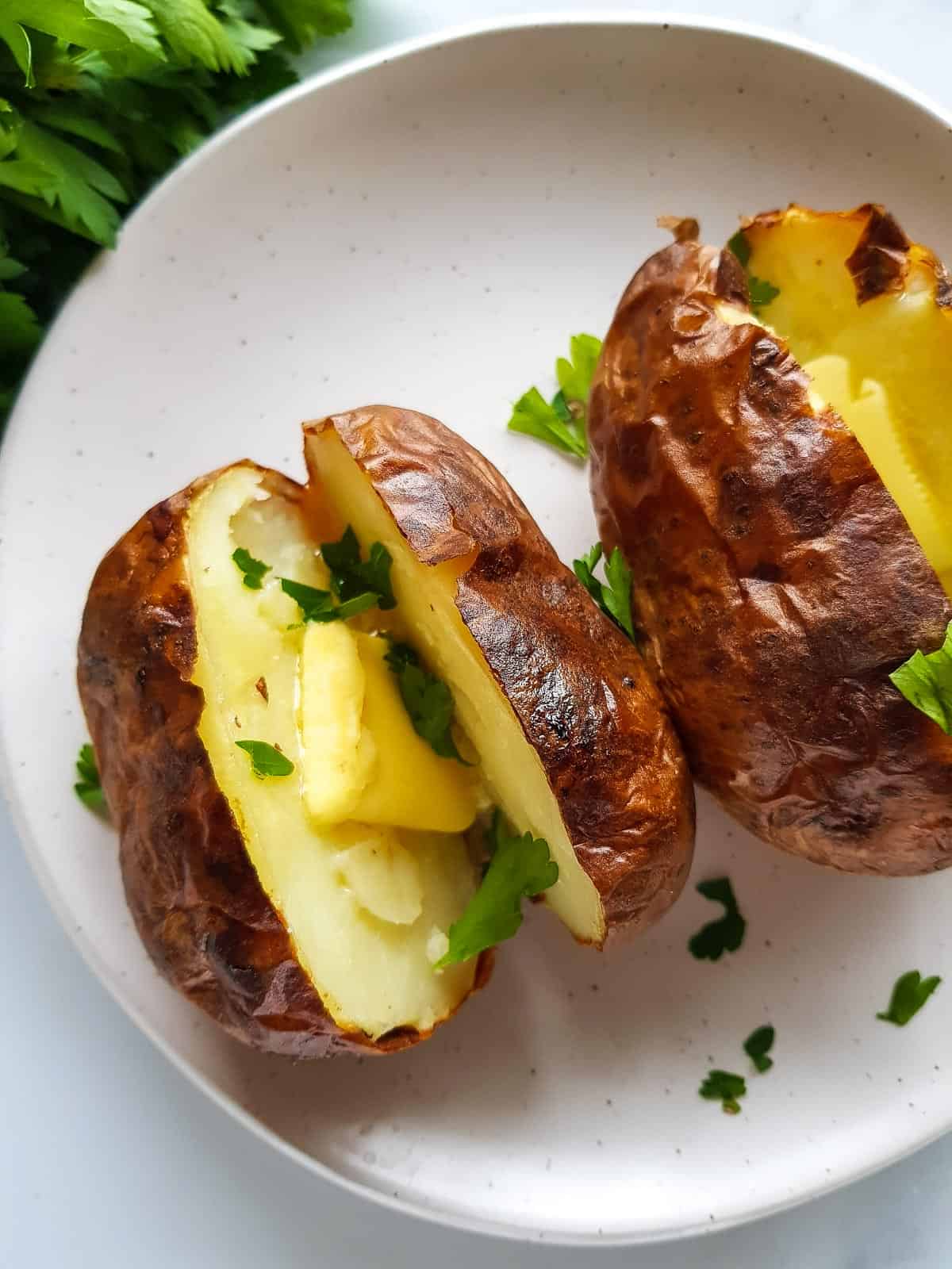 A baked potato with butter and parsley on a plate.