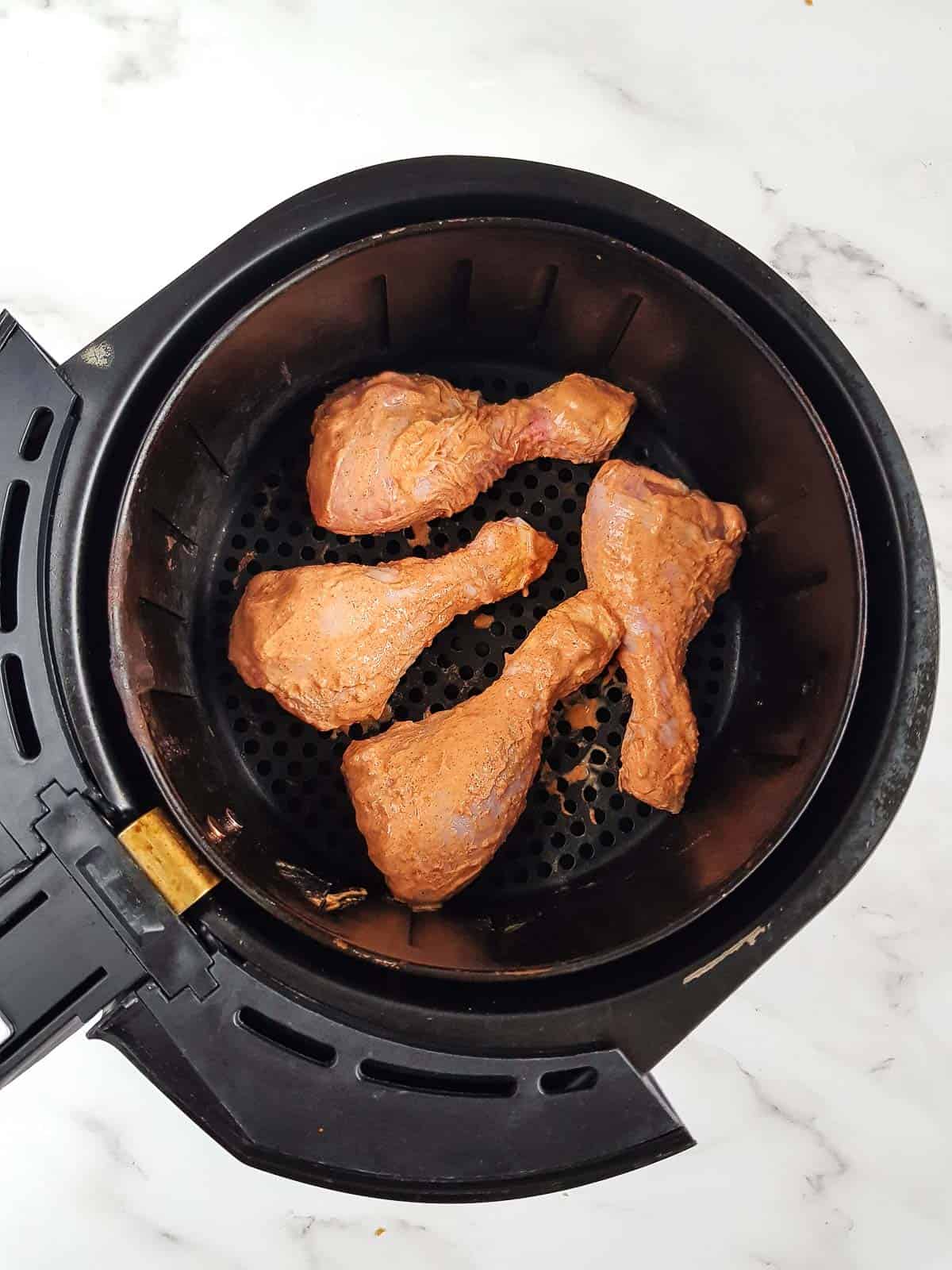 Raw drumsticks in an air fryer.