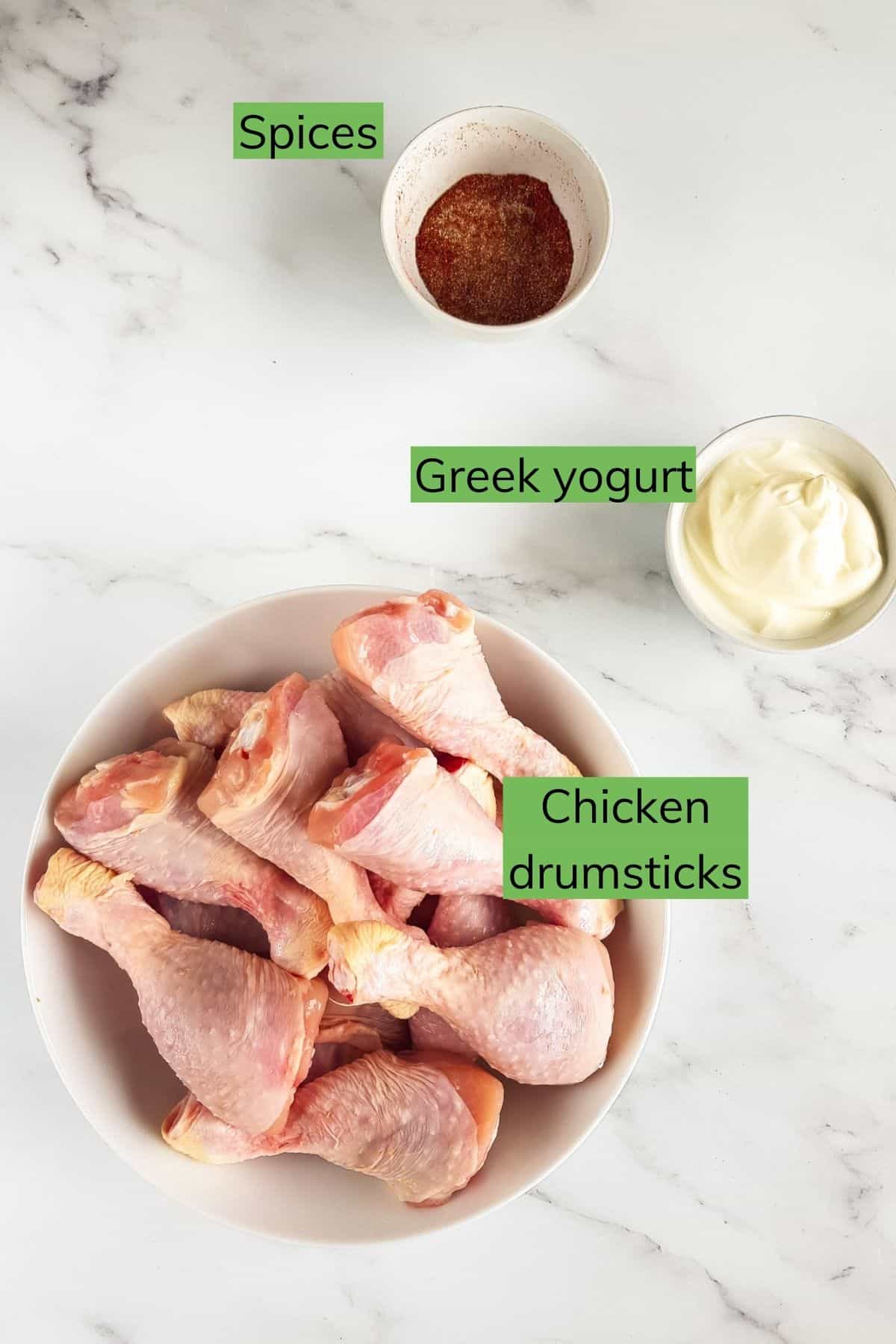 Spices, greek yogurt and raw drumsticks on a table.