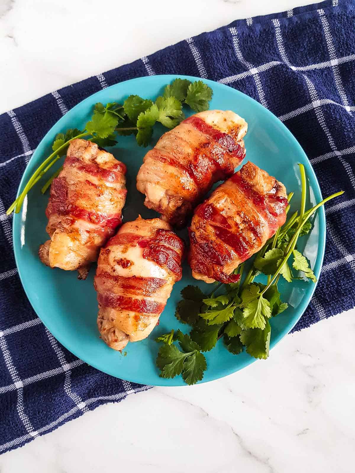 A plate with four bacon wrapped chicken thighs.
