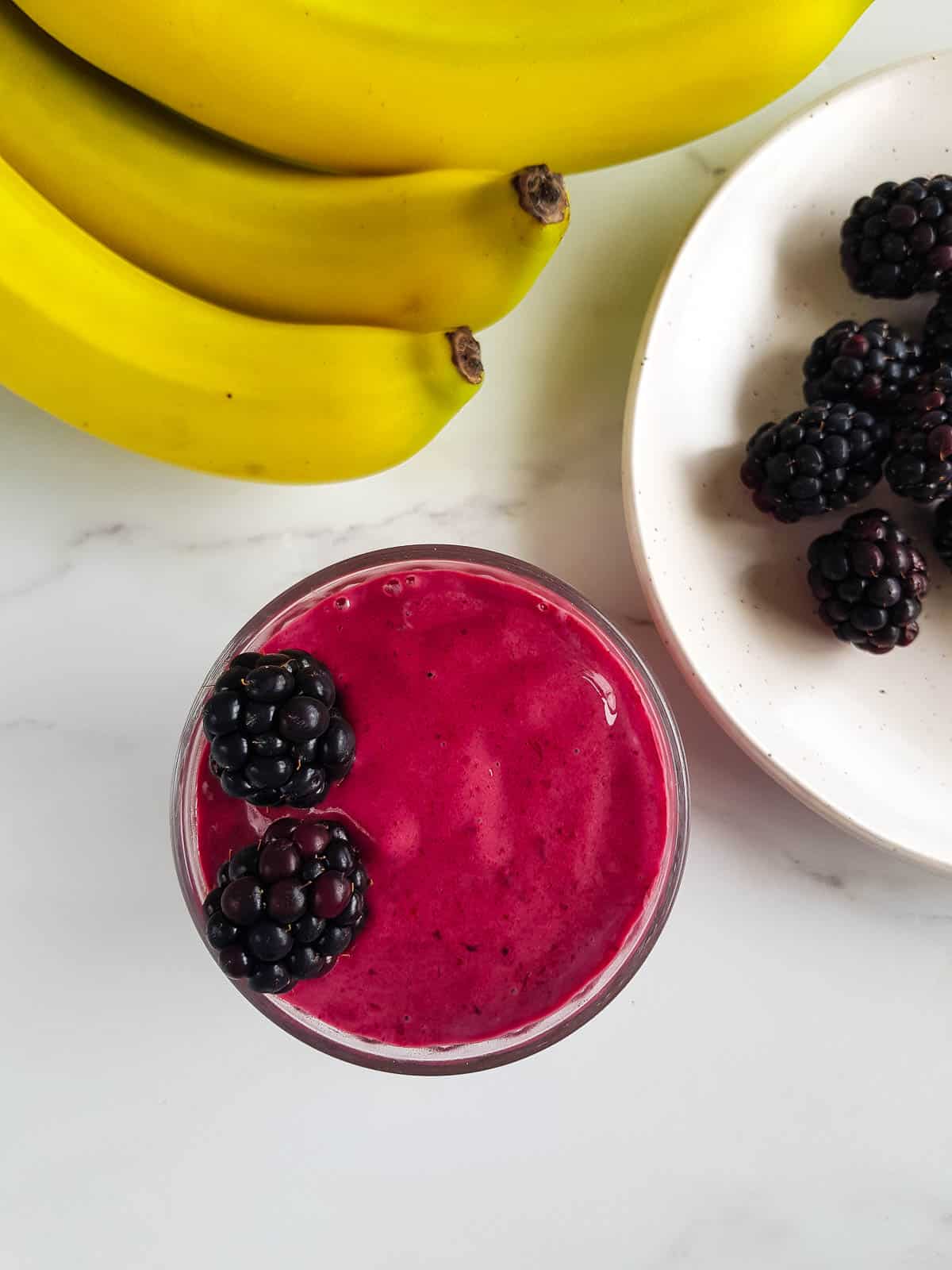 Glass of smoothie with bananas and blackberries on the side.