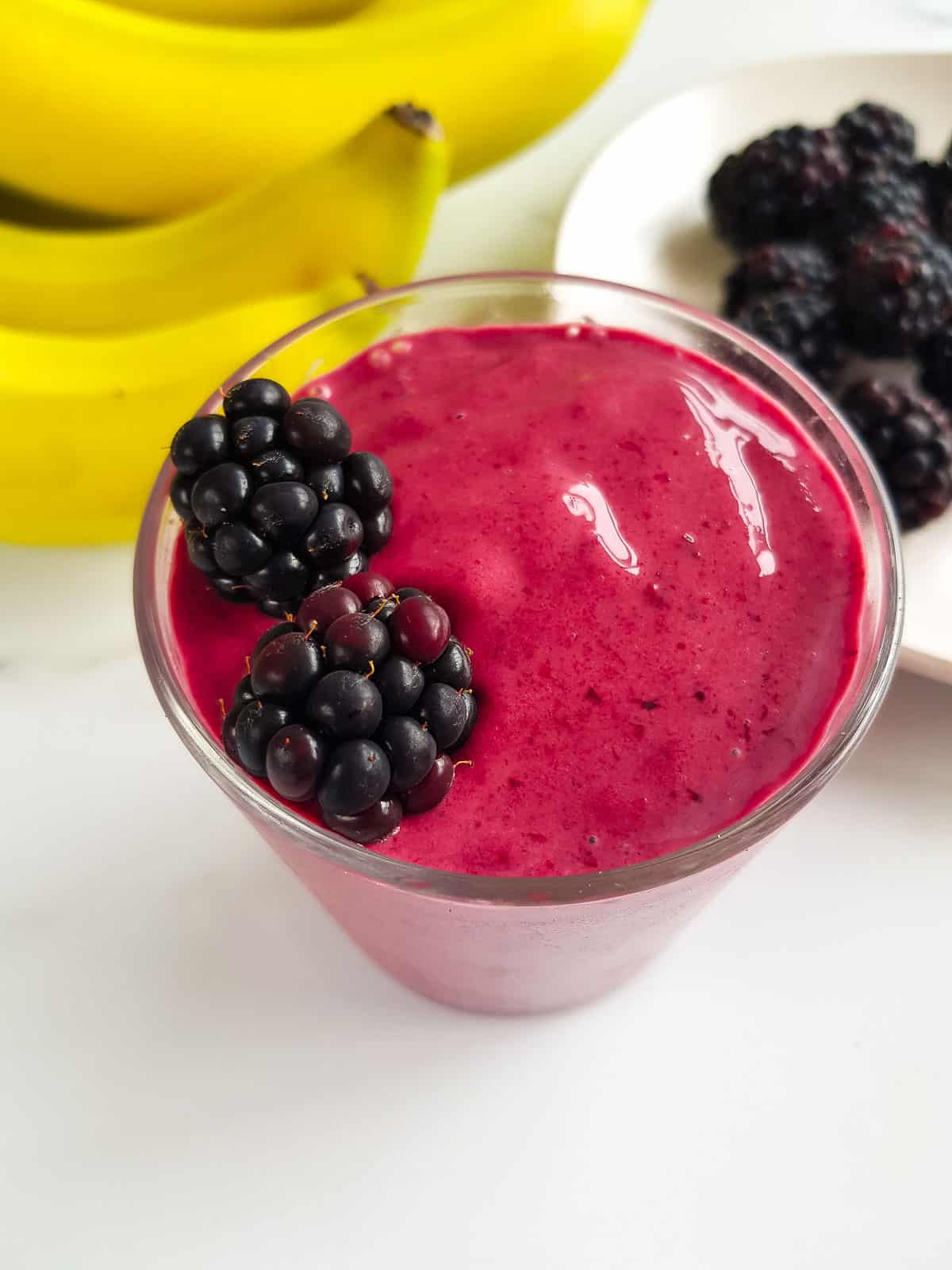 A close up picture of a banana blackberry smoothie with blackberries on top.