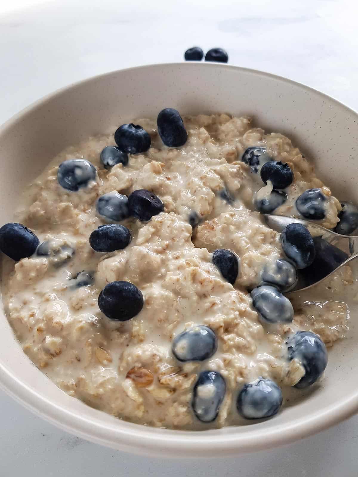 Blueberry overnight oats in a bowl, with a spoon grabbing a serving.