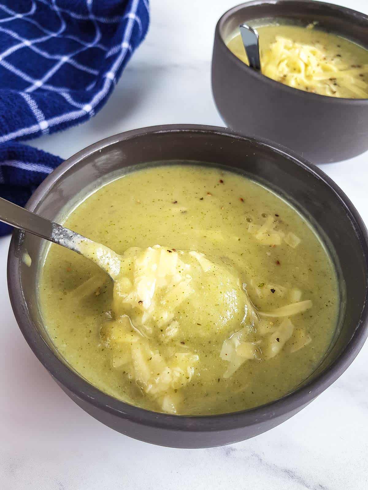 A bowl of broccoli cauliflower soup, with a spoon stirring it.