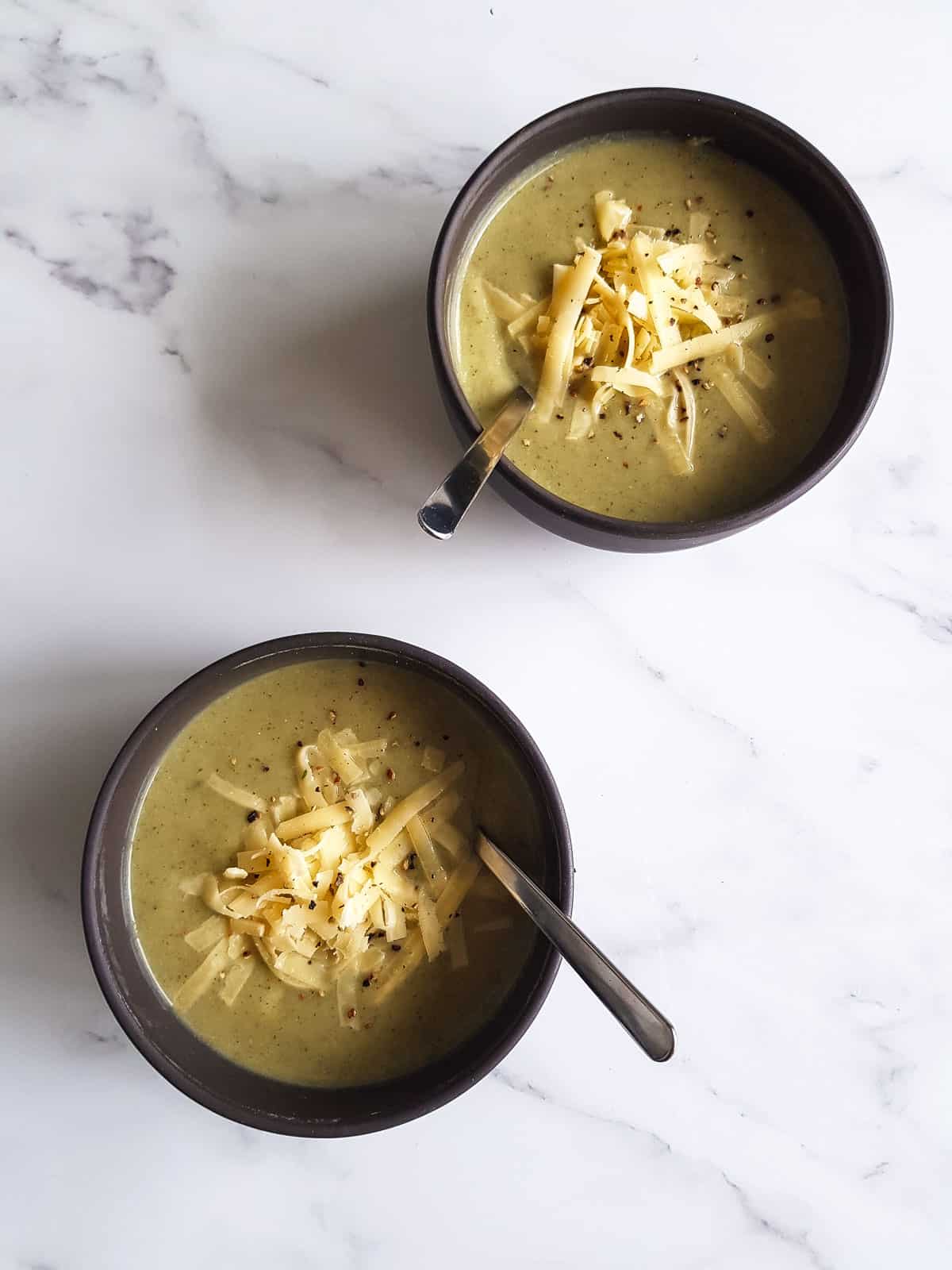 Two bowls of cauliflower broccoli soup with spoons in them.