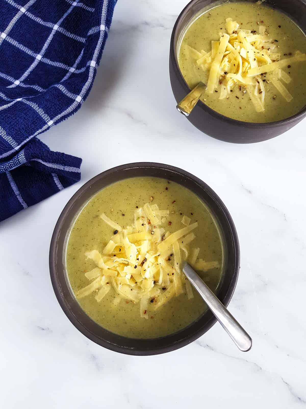 Broccoli and cauliflower soup in bowls with shredded cheese on top.