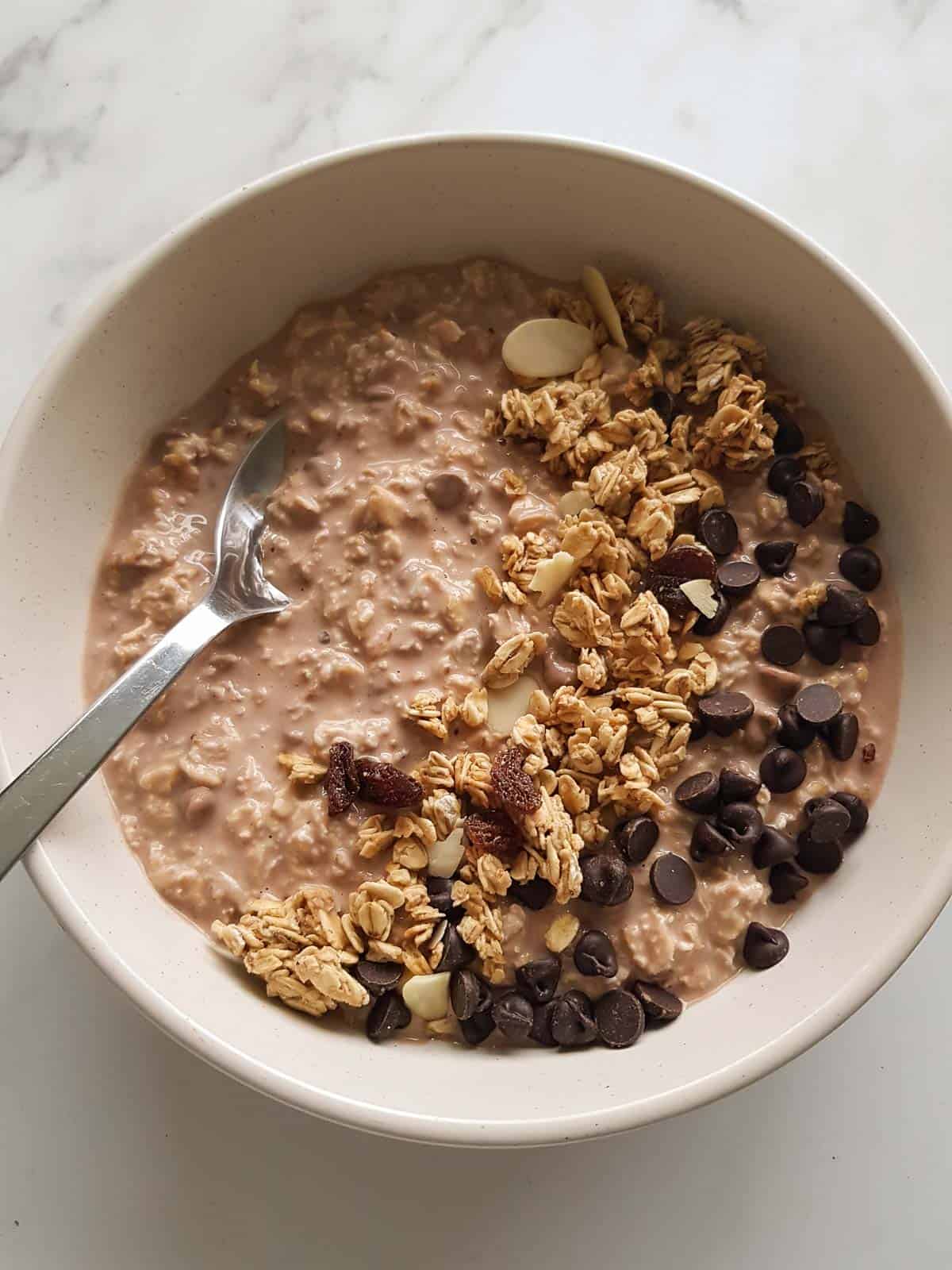 Chocolate chip oats topped with granola - with a spoon placed in the bowl.