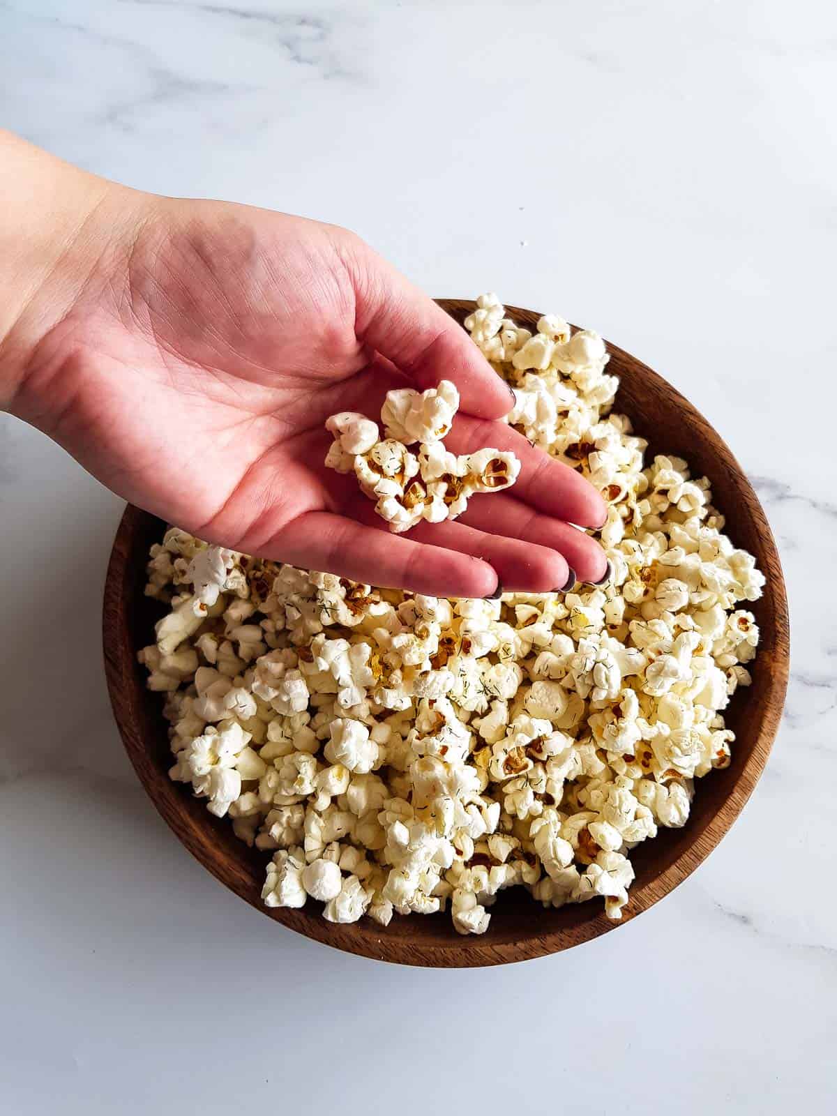 A hand grabbing a portion of popcorn from a wooden bowl.