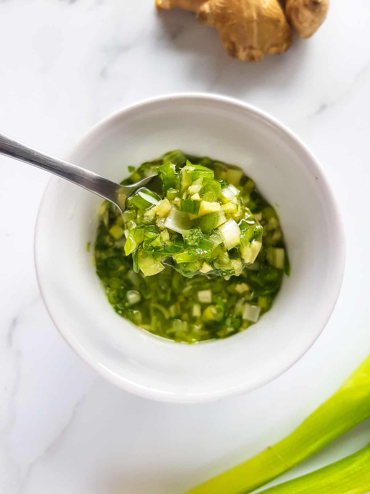 Ginger scallion sauce in a bowl, with a spoon lifting up a serving.