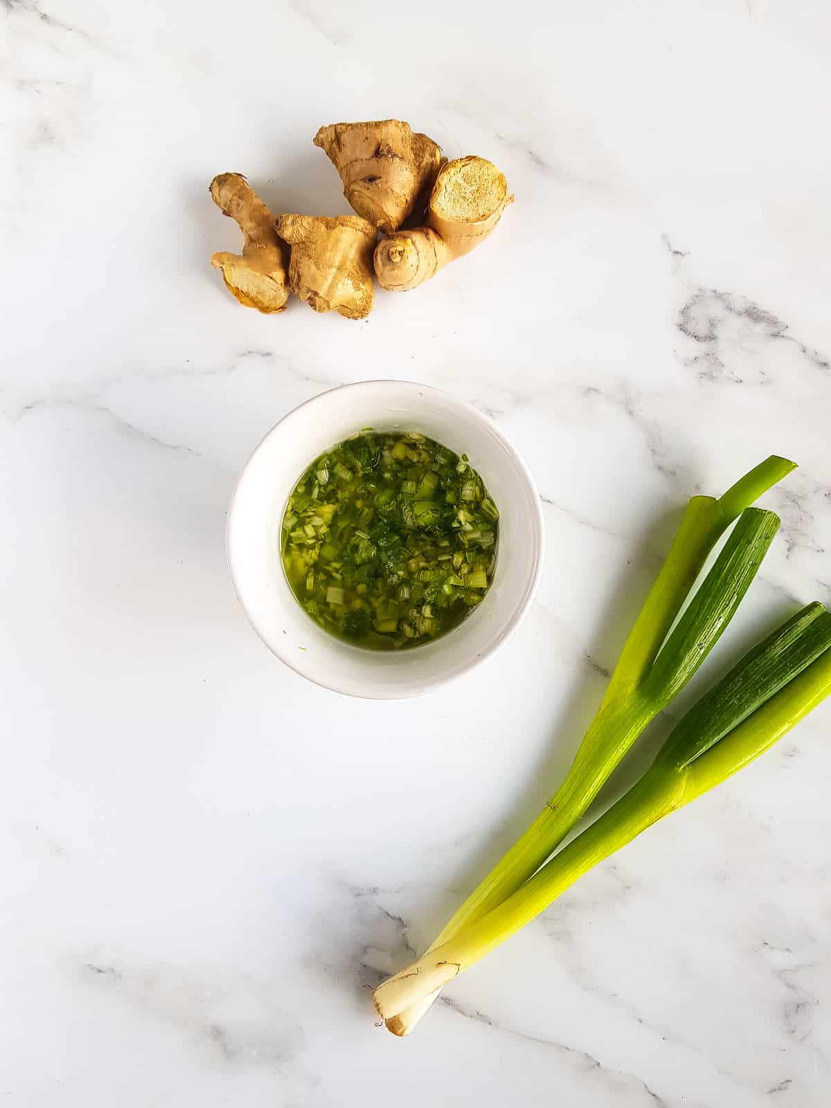 A bowl of ginger sauce with ginger and scallions on the side.