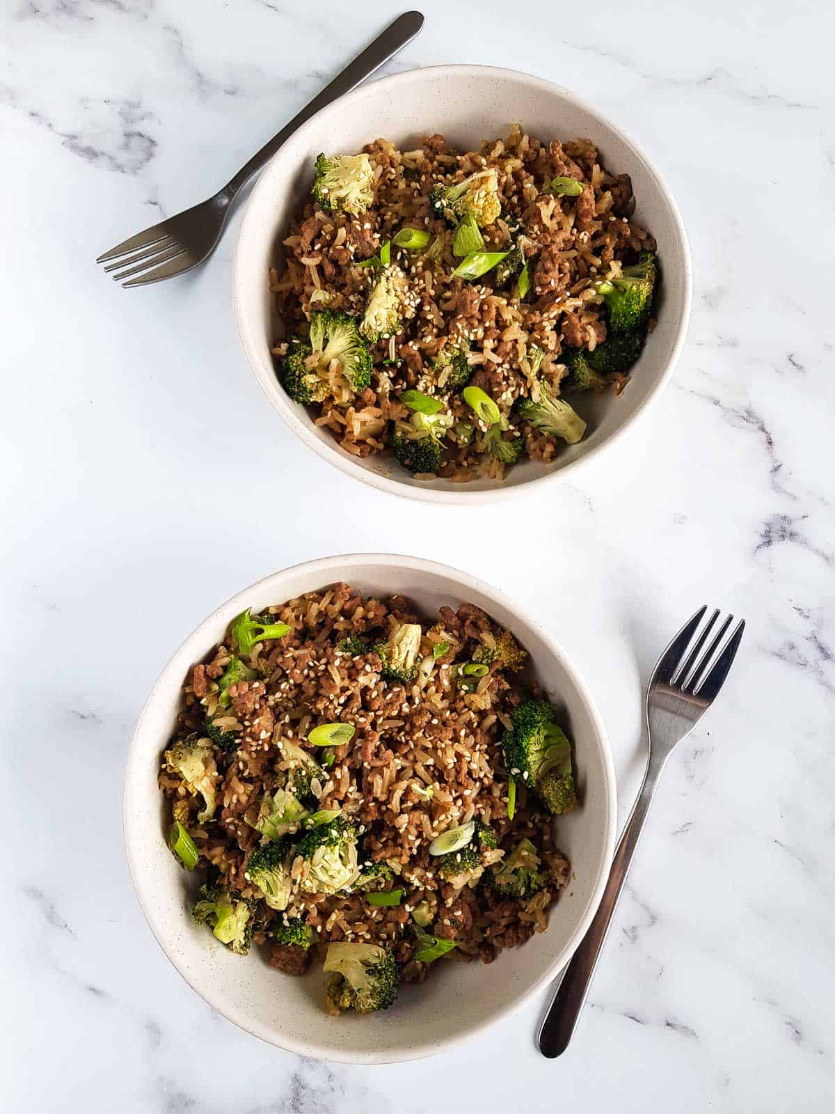 Two bowls of ground beef and broccoli on a table, with forks next to them.