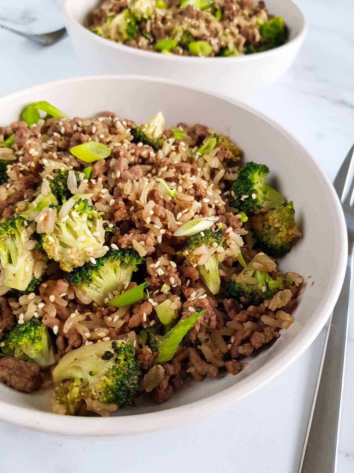 A bowl of rice, beef and broccoli, with a fork next to it.