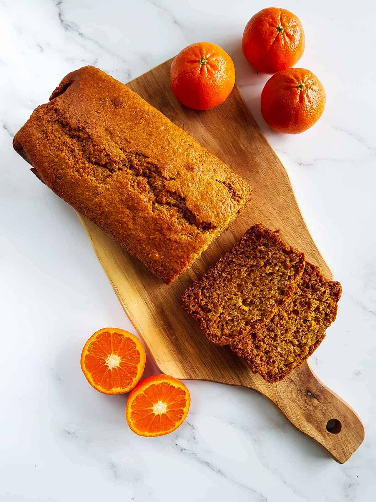 Healthy orange loaf cake on a wooden chopping board, with two slices sliced off.