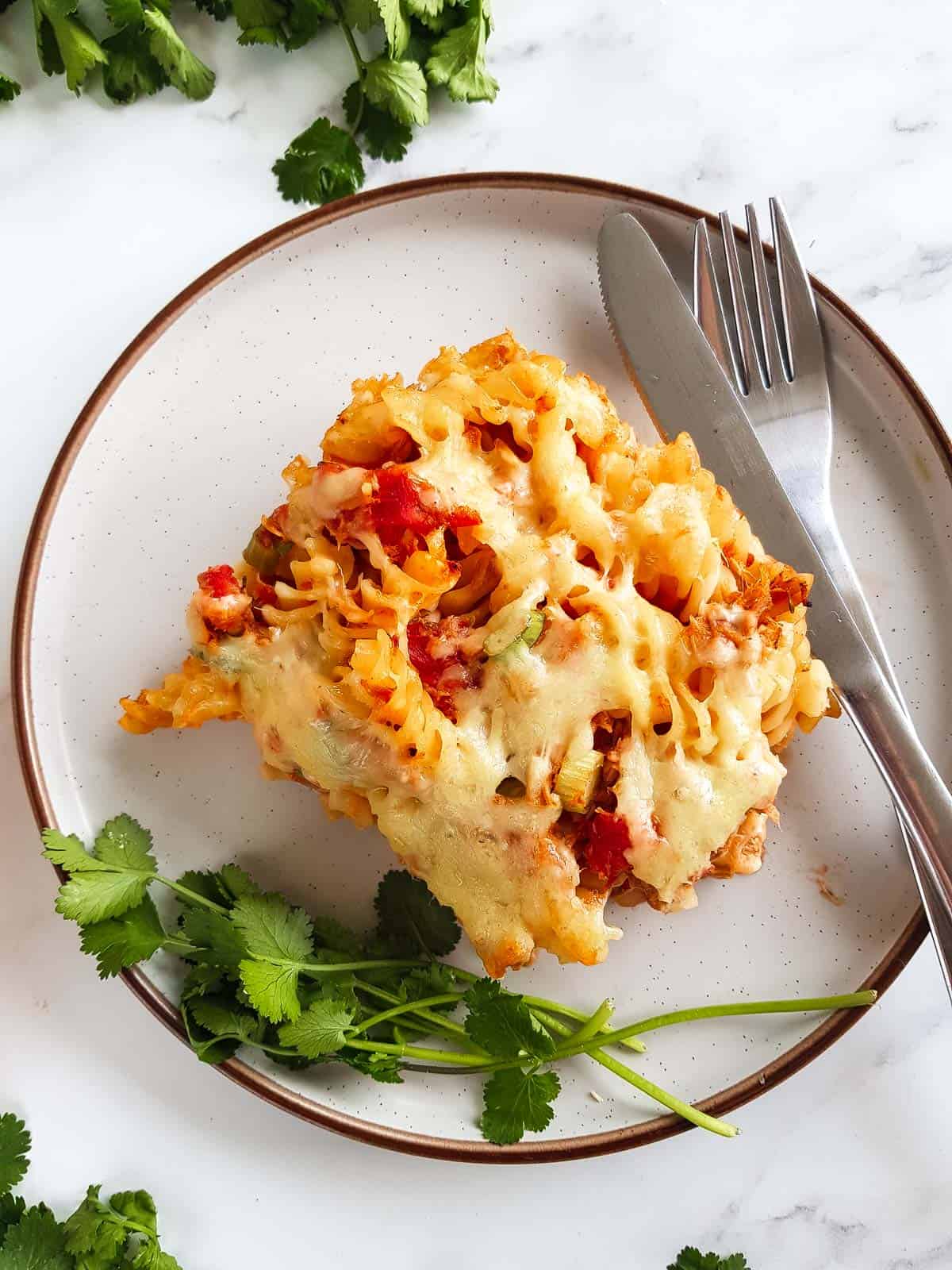 Tuna pasta bake on a plate with cutlery and fresh herbs.