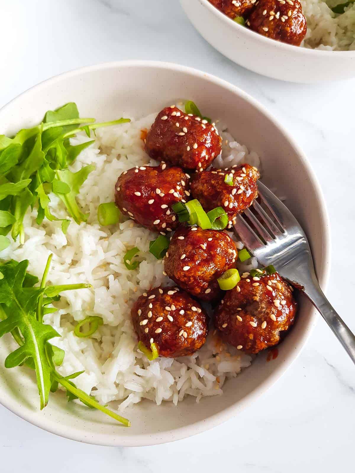 Honey sriracha meatballs in a bowl, with a fork piercing a meatball.