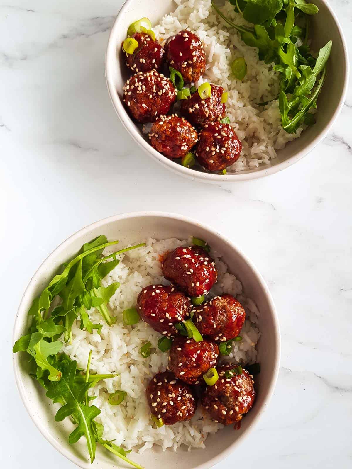 Two bowls of meatballs, rice and arugula.