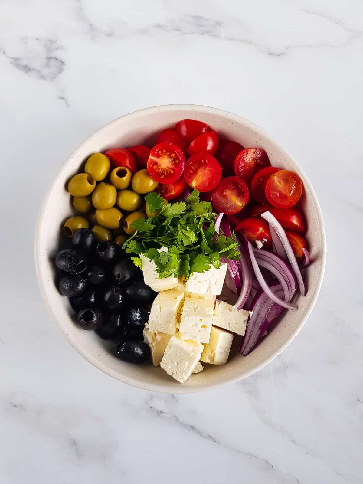 Black and green olives, tomatoes, feta, herbs and red onion in a bowl.